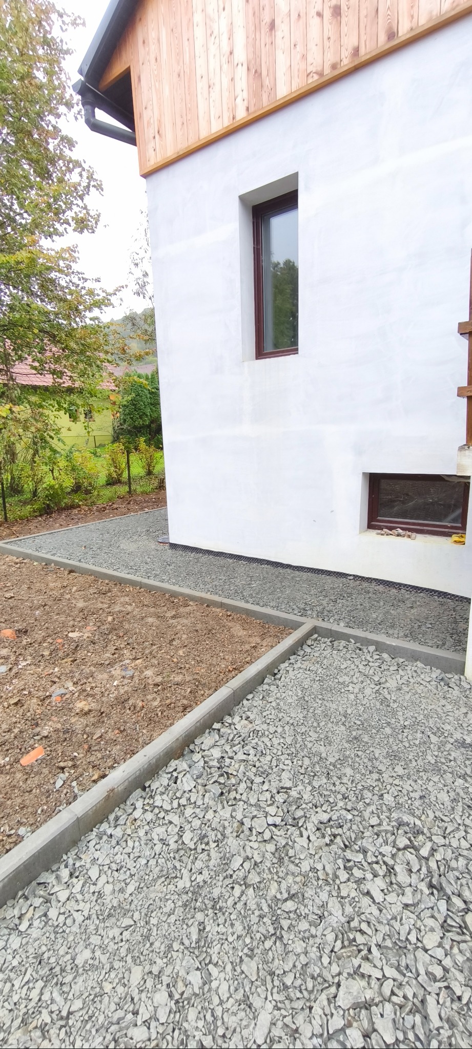 Wykończona ścieżka z kamienia ozdobnego przy białym budynku z drewnianą elewacją. Ułożone obrzeża, widoczny fragment terenu przygotowanego do dalszych prac.