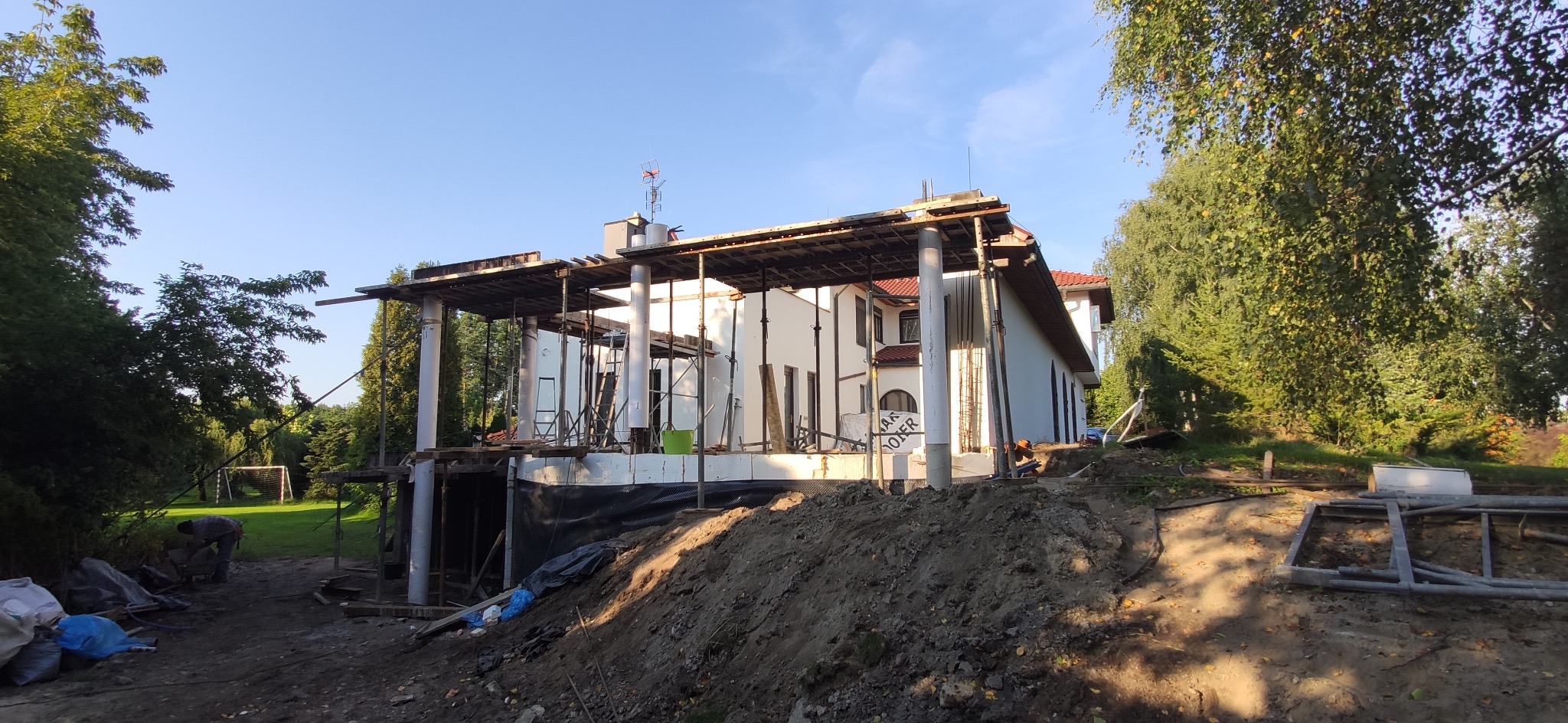 Budowa domu jednorodzinnego w trakcie realizacji: widoczne fundamenty z izolacją, murowane ściany i przygotowanie do wylania stropu. Na pierwszym planie hałda ziemi.