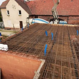 Zbrojenie stropu domu jednorodzinnego z pustaków ceramicznych, widoczny betonowóz z pompą i fragment budynku w tle. Ujęcie z góry, w trakcie prac budowlanych.