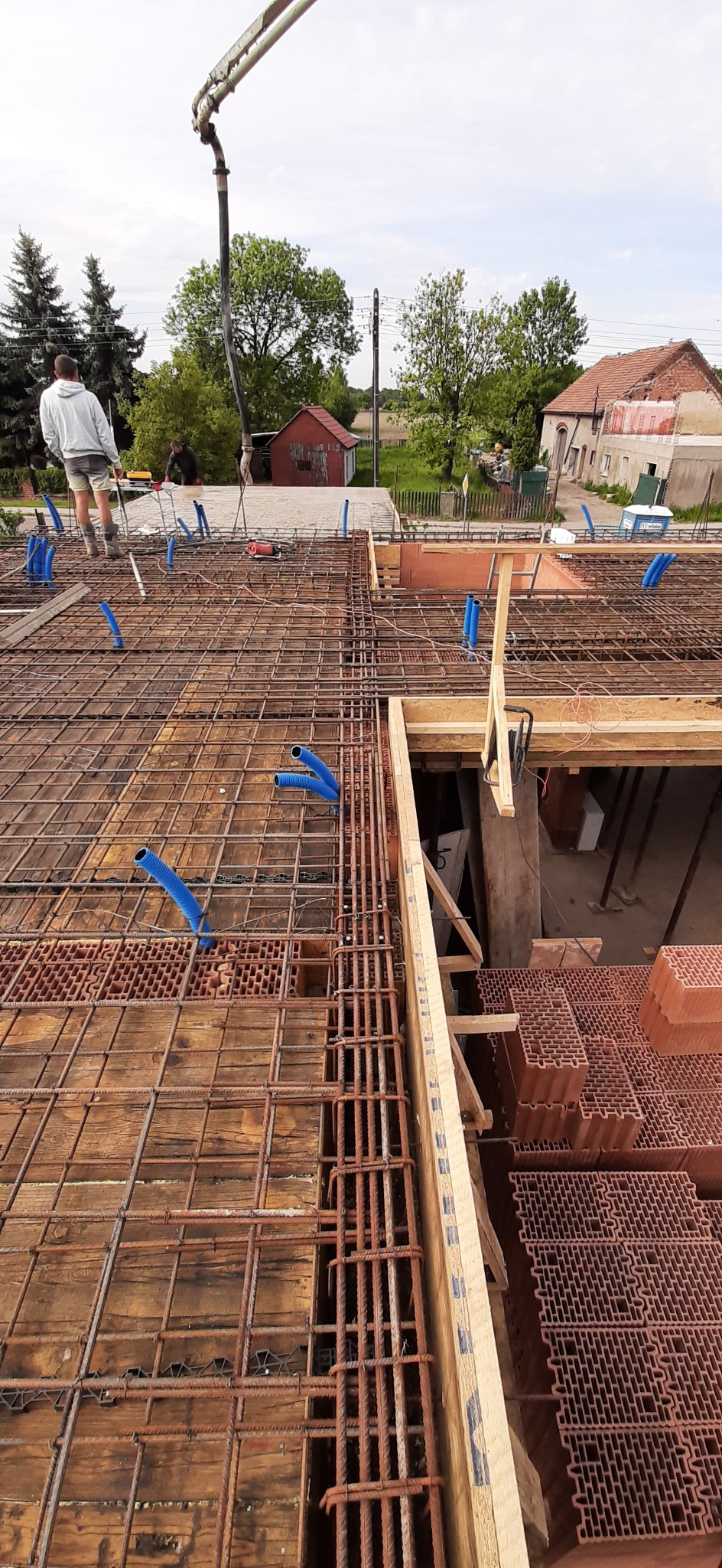 Zbrojenie stropu Teriva z niebieskimi peszlami instalacji elektrycznej. Widoczny beton pompowany. Prace budowlane w toku, widok z góry na konstrukcję.