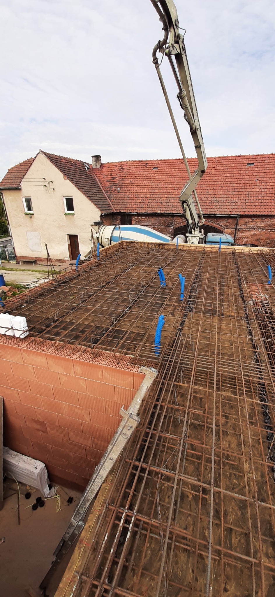 Zbrojenie stropu domu jednorodzinnego z pustaków ceramicznych, widoczny betonowóz z pompą i fragment budynku w tle. Ujęcie z góry, w trakcie prac budowlanych.