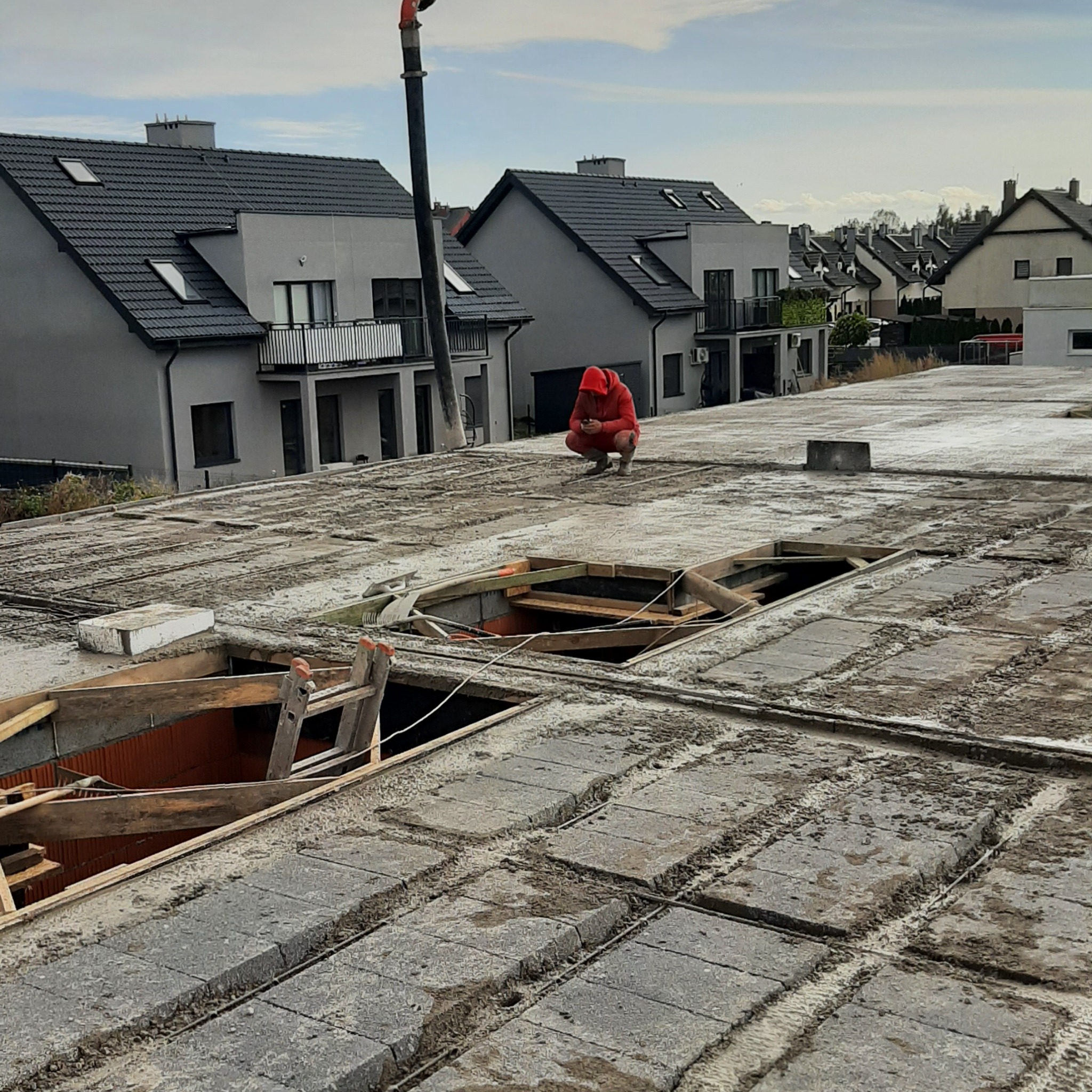 Budowa stropu Teriva z pracownikiem w czerwonej bluzie na tle domów. Widoczne otwory w stropie i elementy konstrukcyjne.