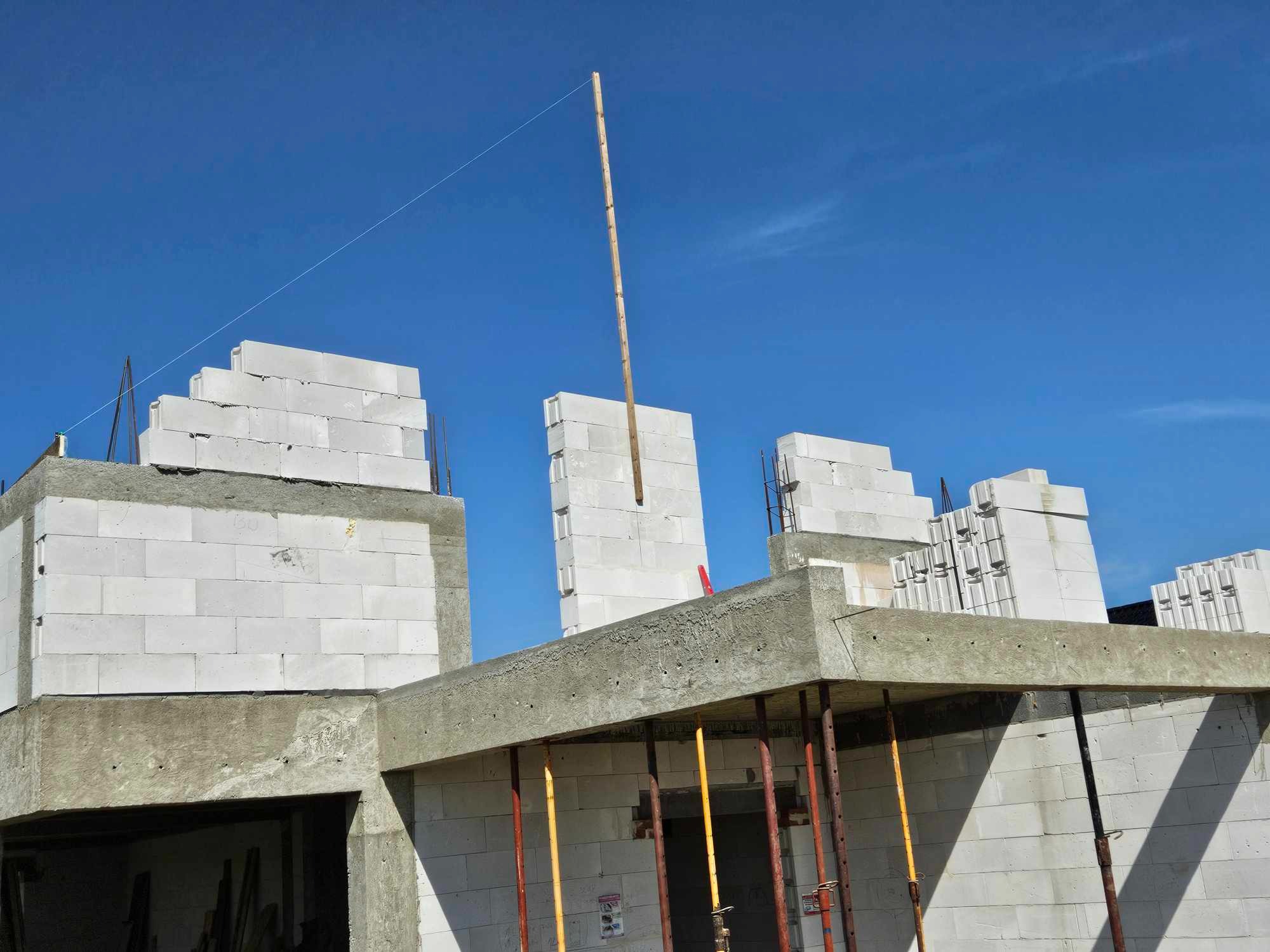 Wznoszenie ścian z bloczków betonu komórkowego na budowie domu jednorodzinnego. Widoczne podpory stropu i pionowa listwa do wyznaczania poziomu.