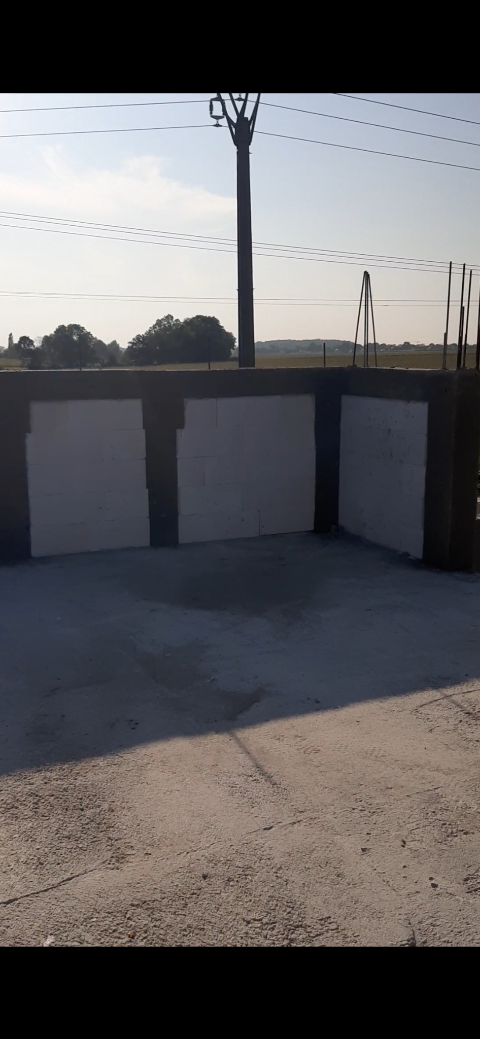 Wznoszenie ścian z bloczków na fundamencie w Wrocławiu. Widoczny krajobraz w tle, słup wysokiego napięcia. Prace murarskie w toku.