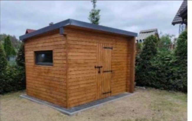 Nowoczesna, drewniana konstrukcja z oknem i drzwiami na zawiasach, otoczona zielenią, z szarą obwódką u podstawy i na dachu.