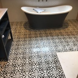 Tomasz Jarosz - Czarno-biała łazienka z wolnostojącą wanną na tle wzorzystej podłogi i ściany wyłożonej białymi płytkami w jodełkę.