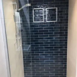 Kabina prysznicowa z ciemnoniebieskimi, błyszczącymi płytkami ułożonymi w cegiełkę, wnęka z podświetleniem, chromowana armatura i odpływ liniowy w podłodze.