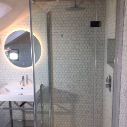 Tomasz Jarosz - Nowoczesna łazienka na poddaszu z kabiną prysznicową ze szklanymi drzwiami, umywalką na metalowym stelażu i okrągłym lustrem z podświetleniem LED, wykończona białymi heksagonalnymi płytkami...