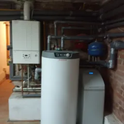 Nowoczesny piec gazowy Immergas, zasobnik ciepłej wody i zmiękczacz wody w kotłowni z widocznymi rurami grzewczymi i instalacją hydrauliczną.