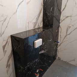 CEGIEŁKA Tomasz Goździela - Wykończona łazienka z czarno-białymi płytkami imitującymi marmur. Widoczna zabudowa stelaża WC z czarnych płyt. Na podłodze szare płytki. Użyto środka do czyszczenia.