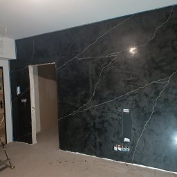 CEGIEŁKA Tomasz Goździela - Ściana w pokoju po malowaniu dekoracyjnym w odcieniach czerni z białymi żyłkami, widoczne puszki elektryczne i fragment drabiny.