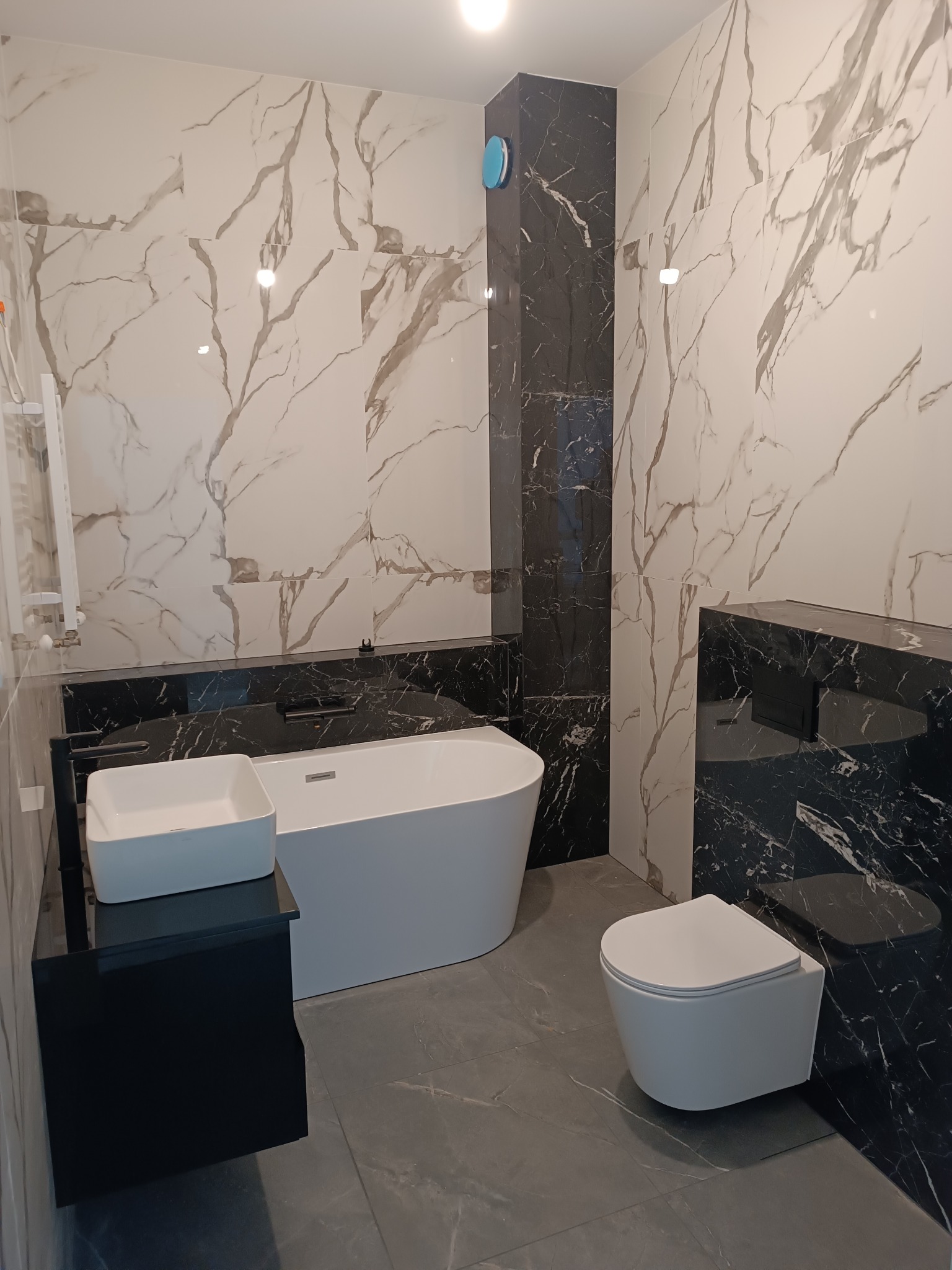 Elegancka łazienka z marmurowymi płytkami w odcieniach bieli i czerni, wolnostojąca wanna, umywalka nablatowa i podwieszana toaleta. Nowoczesny design.