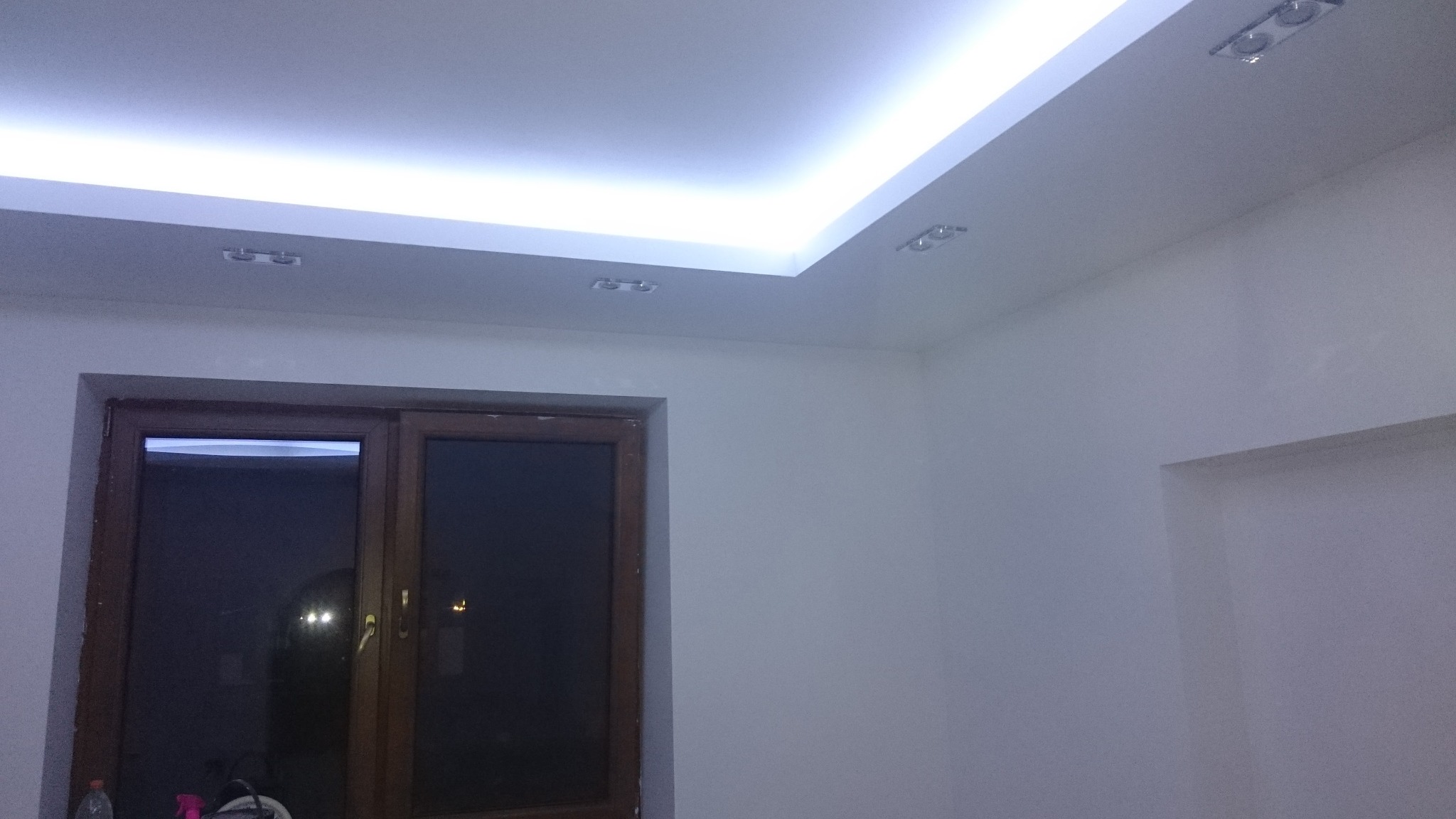 Pokój po remoncie: gładkie, białe ściany, drewniane okno i sufit podwieszany z oświetleniem LED.