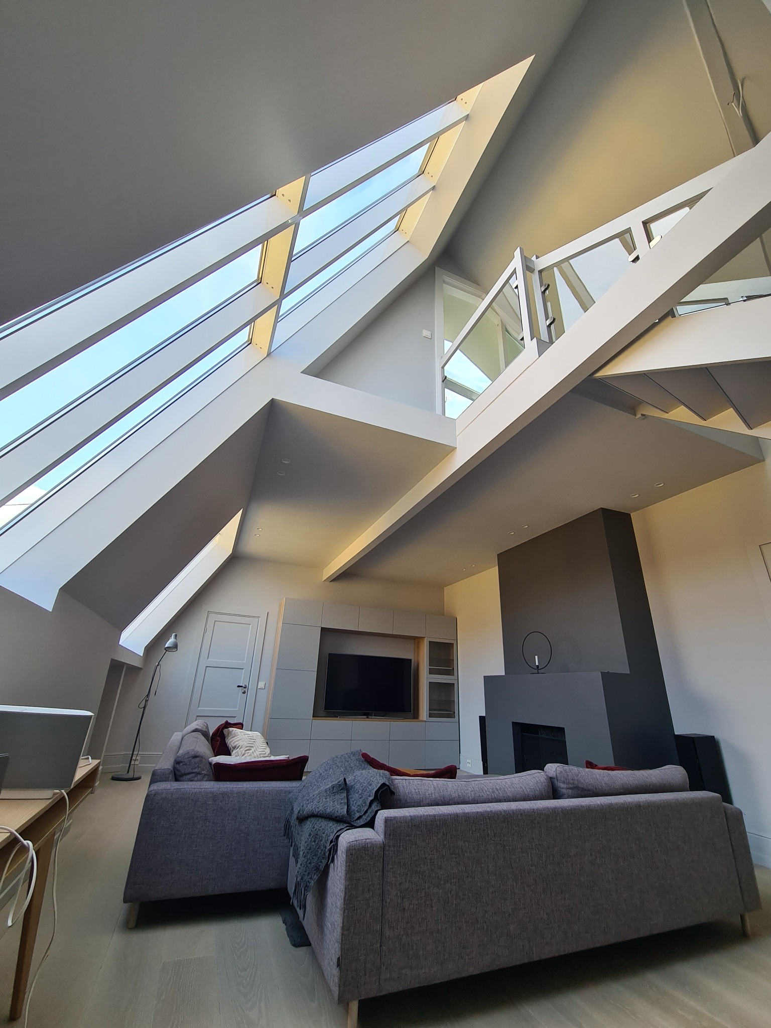 Nowoczesne wnętrze poddasza z dużym oknem dachowym, szarym kominkiem i minimalistycznymi meblami, widok z dołu.