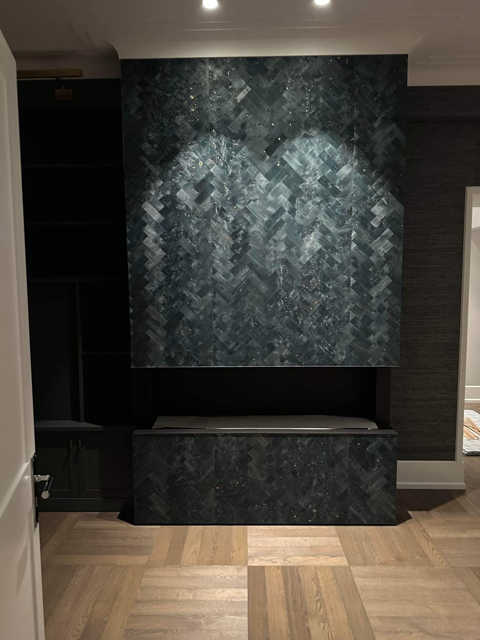 Ściana akcentowa z ciemnozielonej mozaiki ułożonej w jodełkę, z wnęką i szafką, uzupełniona parkietem w jasnym odcieniu drewna.