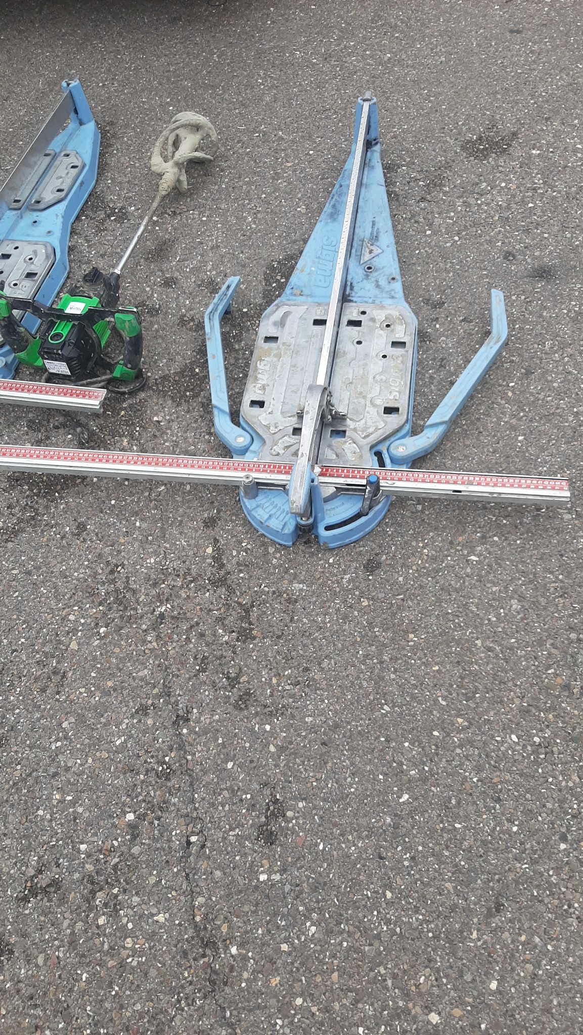 Dwie przecinarki do płytek marki Sigma, zielony laser krzyżowy i mieszadło do zaprawy na szorstkim asfalcie.