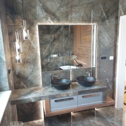 Krystian Ciuruś KRYST-REM - Nowoczesna łazienka z dwoma czarnymi umywalkami nablatowymi, podświetlanym lustrem i marmurowymi płytkami na ścianach i podłodze. Widoczne designerskie lampy wiszące i szafka pod umywalką...