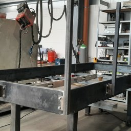 Mobilny Spawacz Jan Bednarczyk Professional Spaw 303 - Konstrukcja metalowa z profili, spawana, w warsztacie. Widoczny spawacz, butle z gazem i regał z narzędziami w tle. Element konstrukcyjny, prawdopodobnie schody lub balustrada.