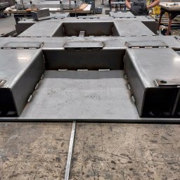 Mobilny Spawacz Jan Bednarczyk Professional Spaw 303 - Spawana konstrukcja stalowa z profili zamkniętych, widoczne spawy i otwory, surowy metal, na stole warsztatowym z śladami użytkowania, w tle warsztat.