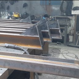 Mobilny Spawacz Jan Bednarczyk Professional Spaw 303 - Metalowe elementy konstrukcyjne w warsztacie, spawarka na stole, widoczne ślady obróbki, surowy, industrialny charakter, elementy do konstrukcji schodów.