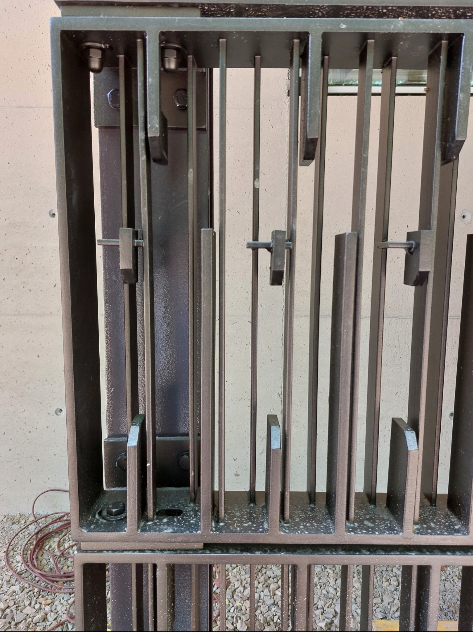 Metalowa konstrukcja bramy wjazdowej w Warszawie, z widocznymi elementami mocującymi i spawami, na tle betonowej ściany. Detal wykonania.