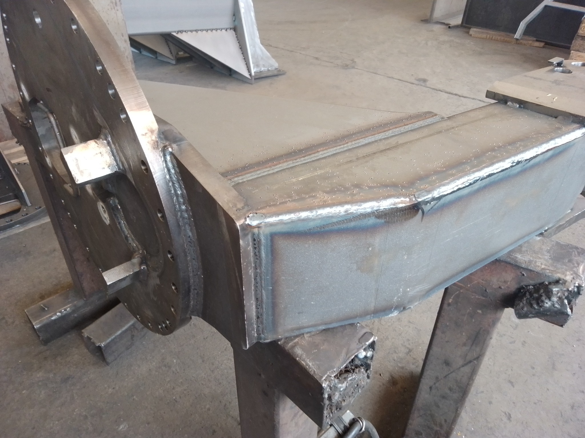 Metalowa konstrukcja spawana, z widocznymi śladami obróbki, umieszczona na metalowych podporach. Widoczne spawy i elementy konstrukcyjne.