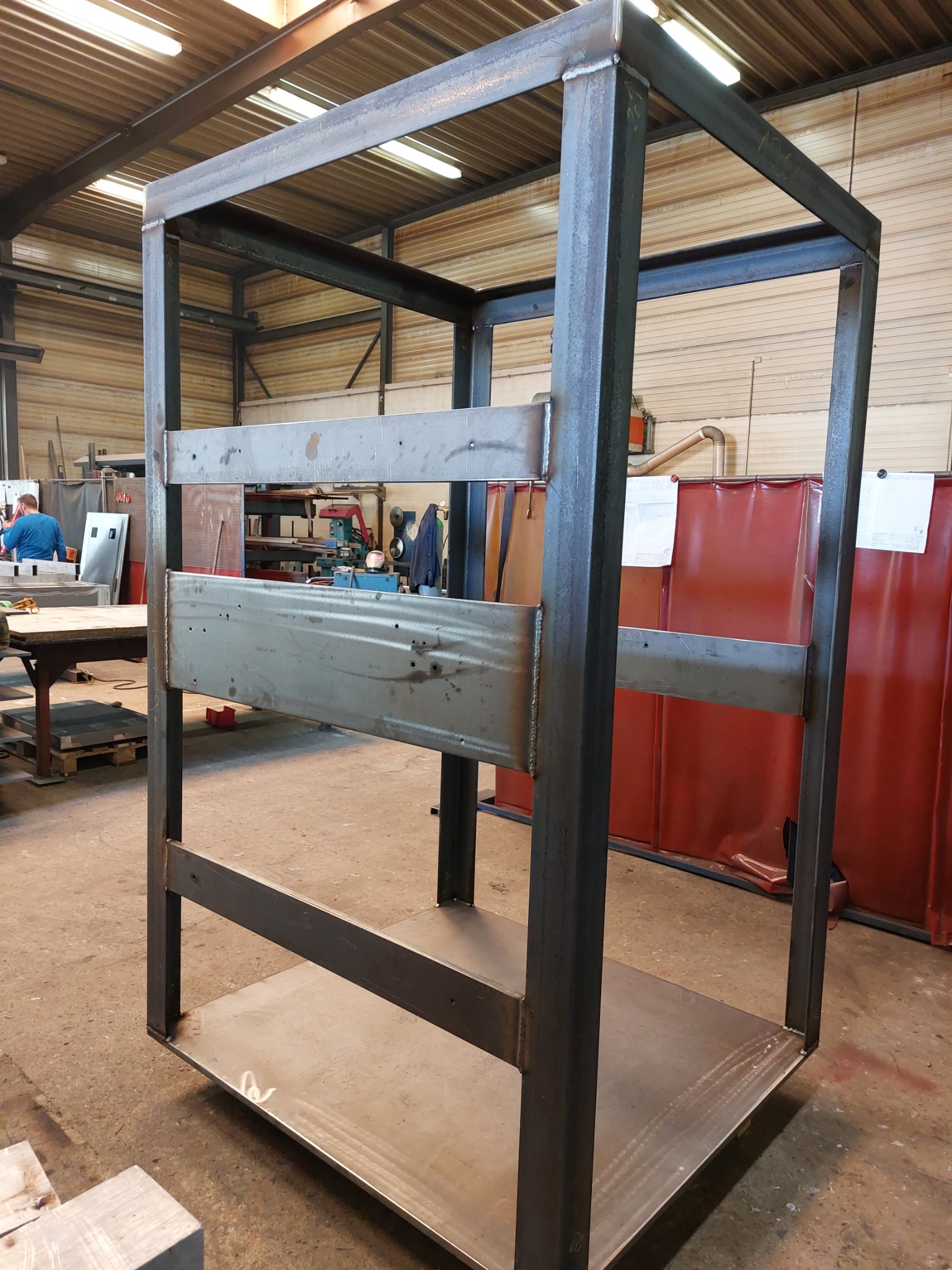 Surowa, spawana konstrukcja stalowa z profili zamkniętych, widoczna w warsztacie. Elementy połączone spawami. Widoczne ślady obróbki i niedoskonałości.