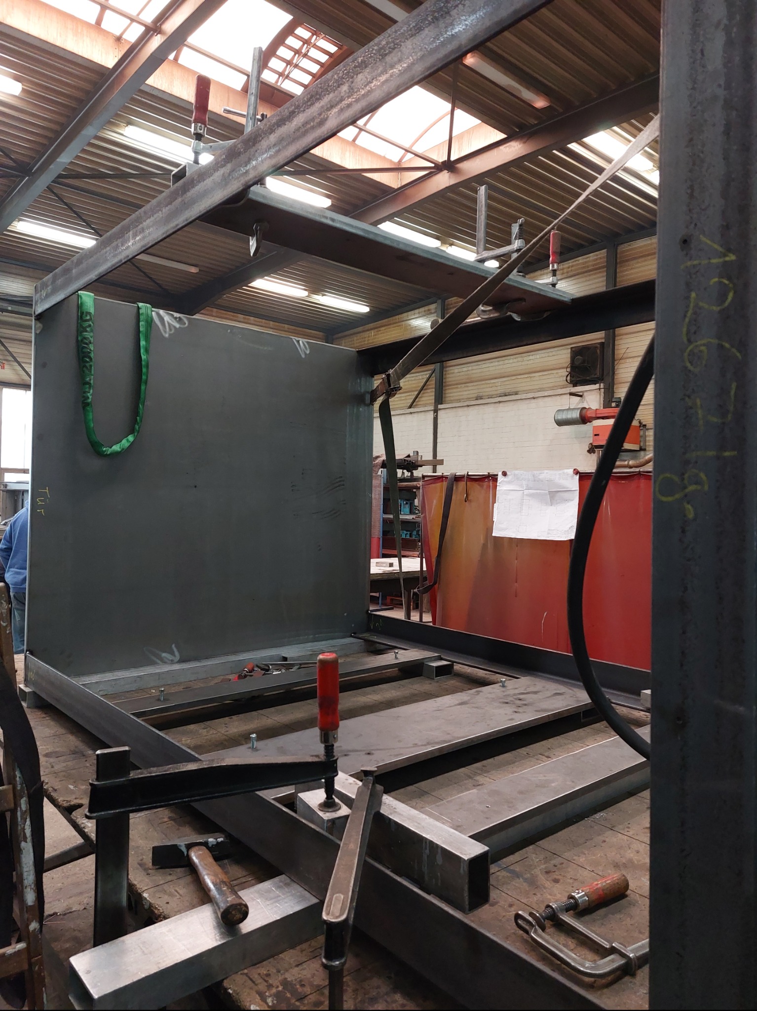 Konstrukcja metalowa w trakcie spawania w warsztacie w Warszawie. Widoczne narzędzia, profile stalowe i element poszycia. Prace spawalnicze w toku.