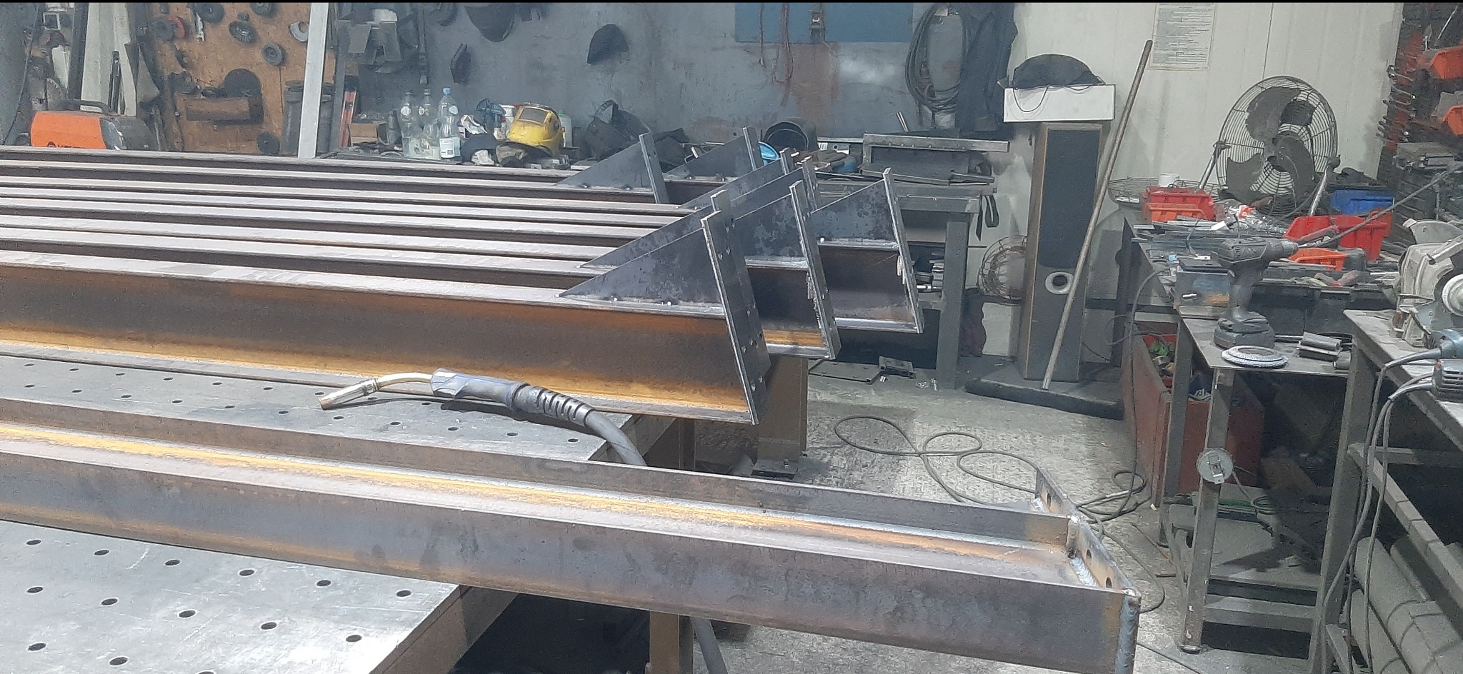 Metalowe elementy konstrukcyjne w warsztacie, spawarka na stole, widoczne ślady obróbki, surowy, industrialny charakter, elementy do konstrukcji schodów.