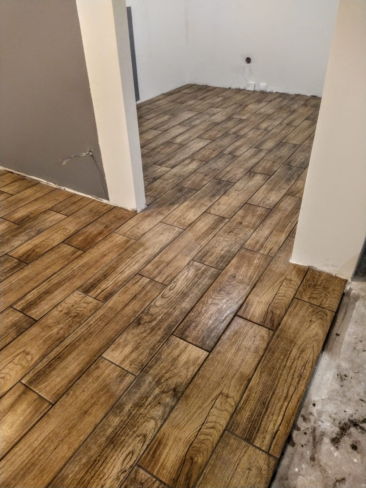Ułożona podłoga z płytek imitujących drewno w nowym wnętrzu, widoczne niedociągnięcia przy ścianie i wystające kable.