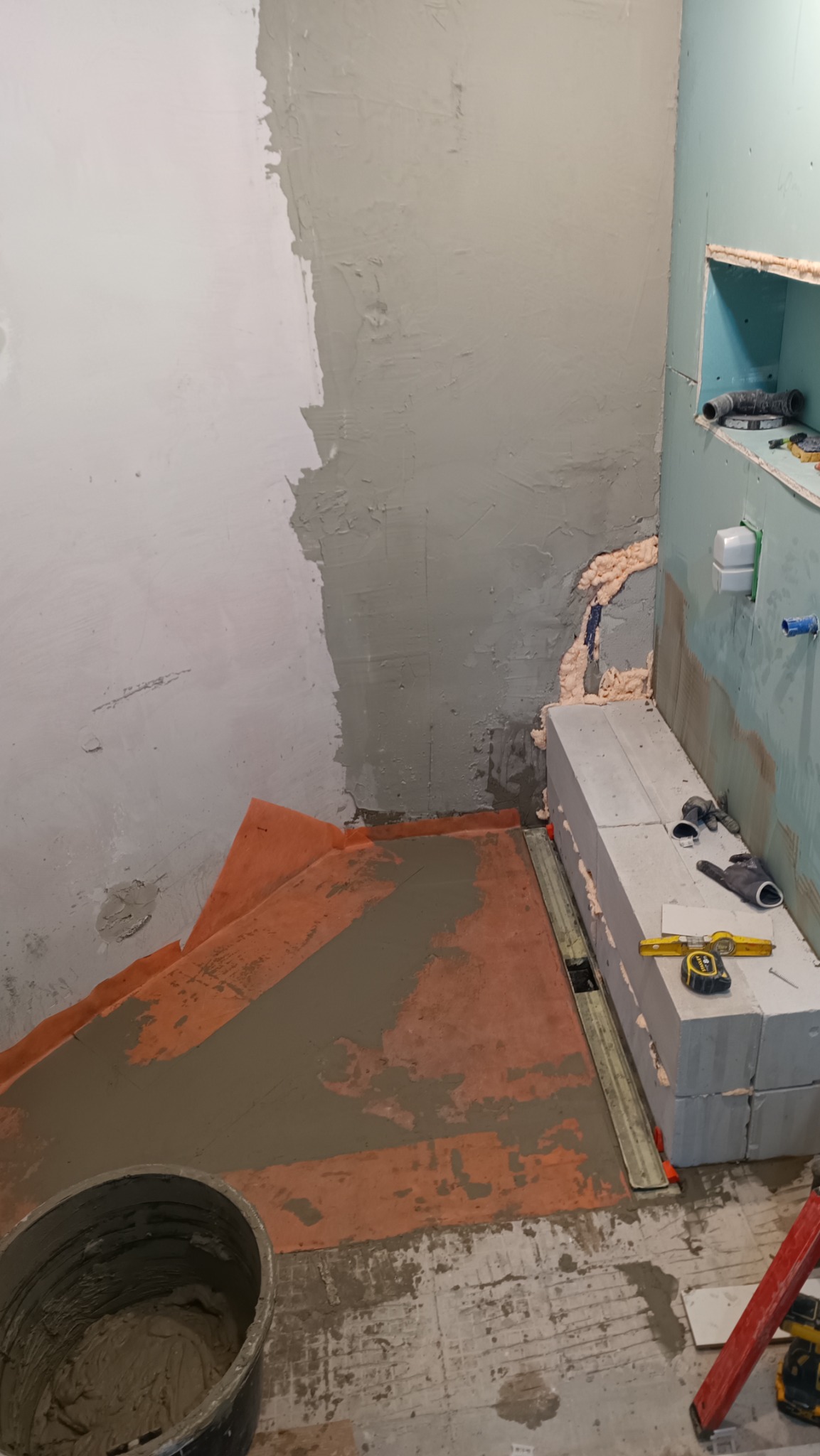 Przygotowanie podłoża pod prysznic typu walk-in: hydroizolacja, wylewka, odpływ liniowy w trakcie montażu, bloczki z betonu komórkowego, poziomica i puszka instalacyjna w tle.