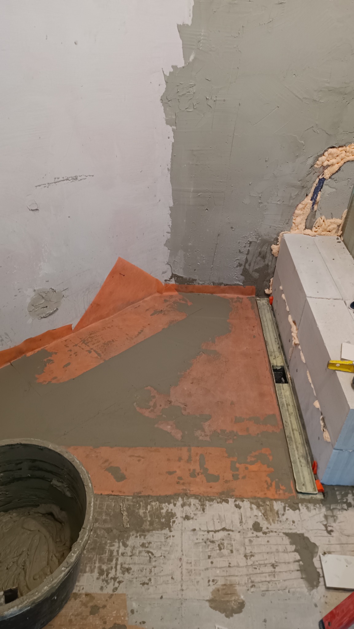 Prace przygotowawcze w Werbkowicach: hydroizolacja podłoża w strefie prysznicowej z widoczną taśmą uszczelniającą, warstwą wylewki i odpływem liniowym.