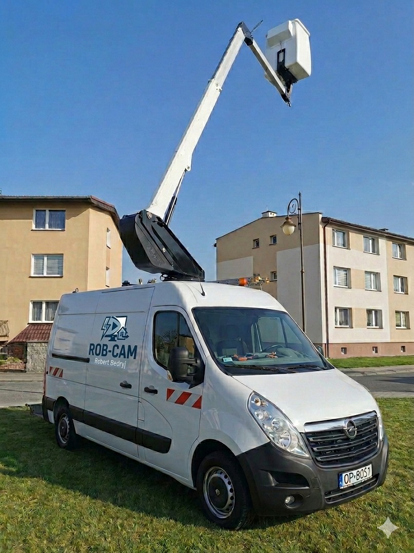 Biały Opel Movano z podnośnikiem koszowym ROB-CAM na tle budynków i błękitnego nieba. Usługi na wysokościach, wsparcie techniczne, instalacje.
