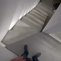 Wnętrze nowoczesnego domu z białymi schodami z podświetleniem LED, widok z góry na stopy osoby stojącej na kafelkach podłogowych.