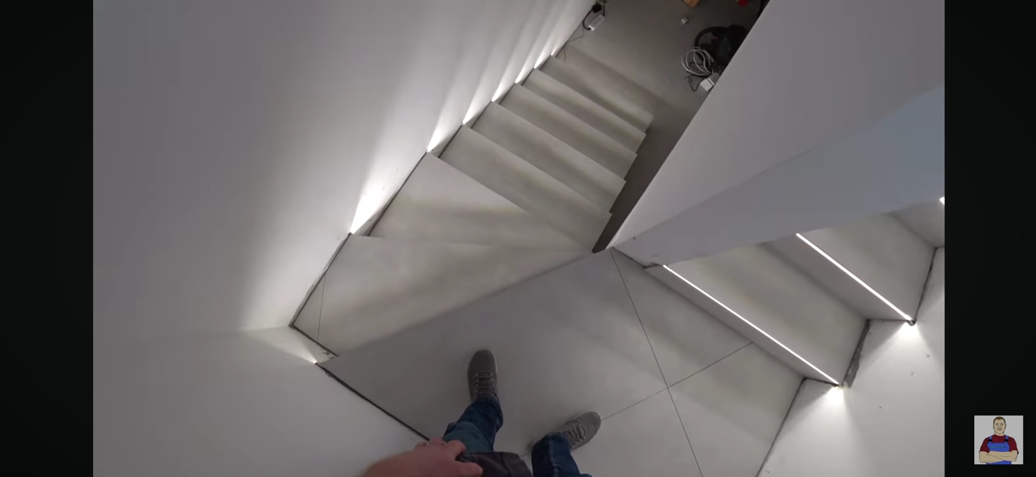 Wnętrze nowoczesnego domu z białymi schodami z podświetleniem LED, widok z góry na stopy osoby stojącej na kafelkach podłogowych.