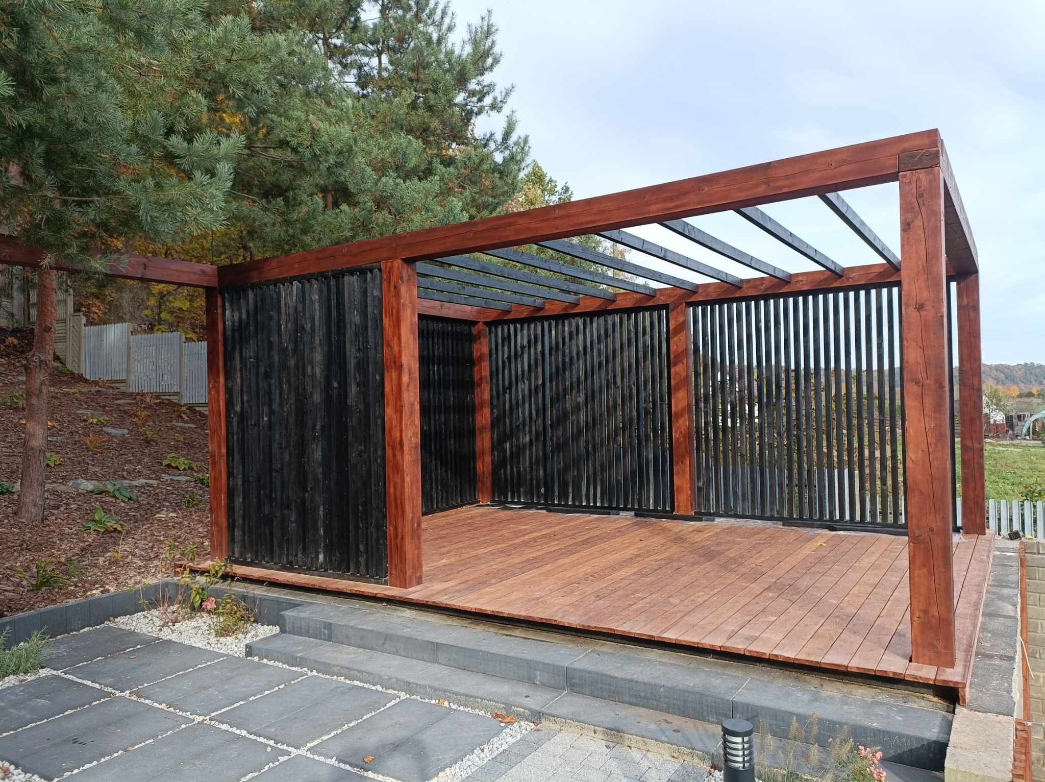 Nowoczesna altana z drewnianą podłogą i czarnymi pionowymi panelami, widok z zewnątrz na tle zieleni i kostki brukowej.