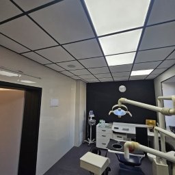Grzegorz Wojdyła Gregor Bau - Nowoczesny gabinet stomatologiczny z ciemną ścianą, białymi meblami i sufitem kasetonowym z podświetleniem LED.