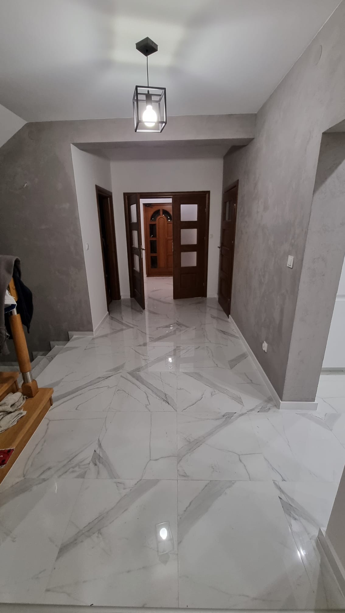 Wnętrze korytarza po remoncie z marmurową posadzką i szarymi ścianami, widoczne drewniane drzwi i nowoczesna lampa sufitowa.
