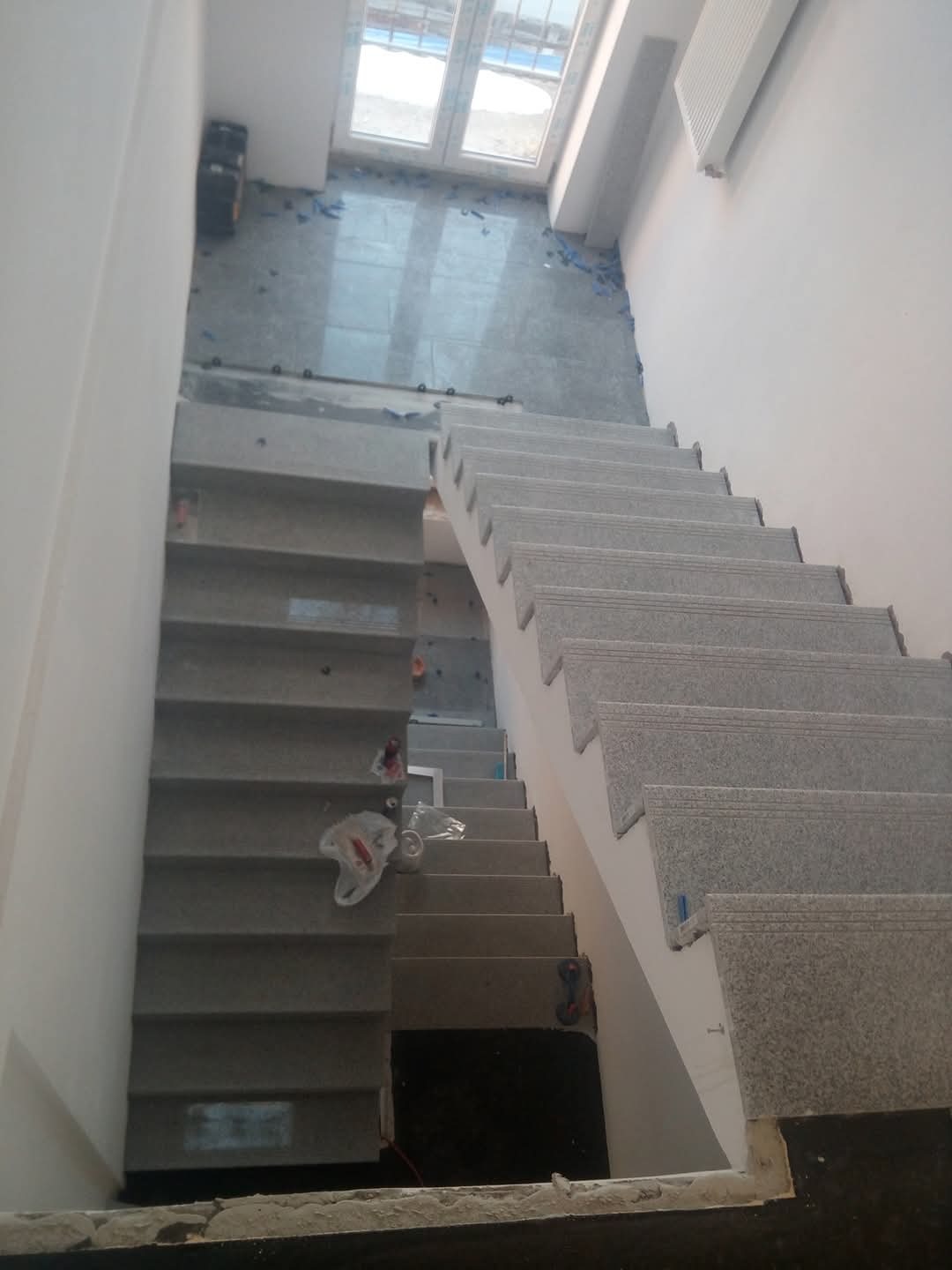 Schody wewnętrzne wyłożone szarym kamieniem, widok z góry, z widocznymi śladami prac wykończeniowych na podłodze i ścianach.