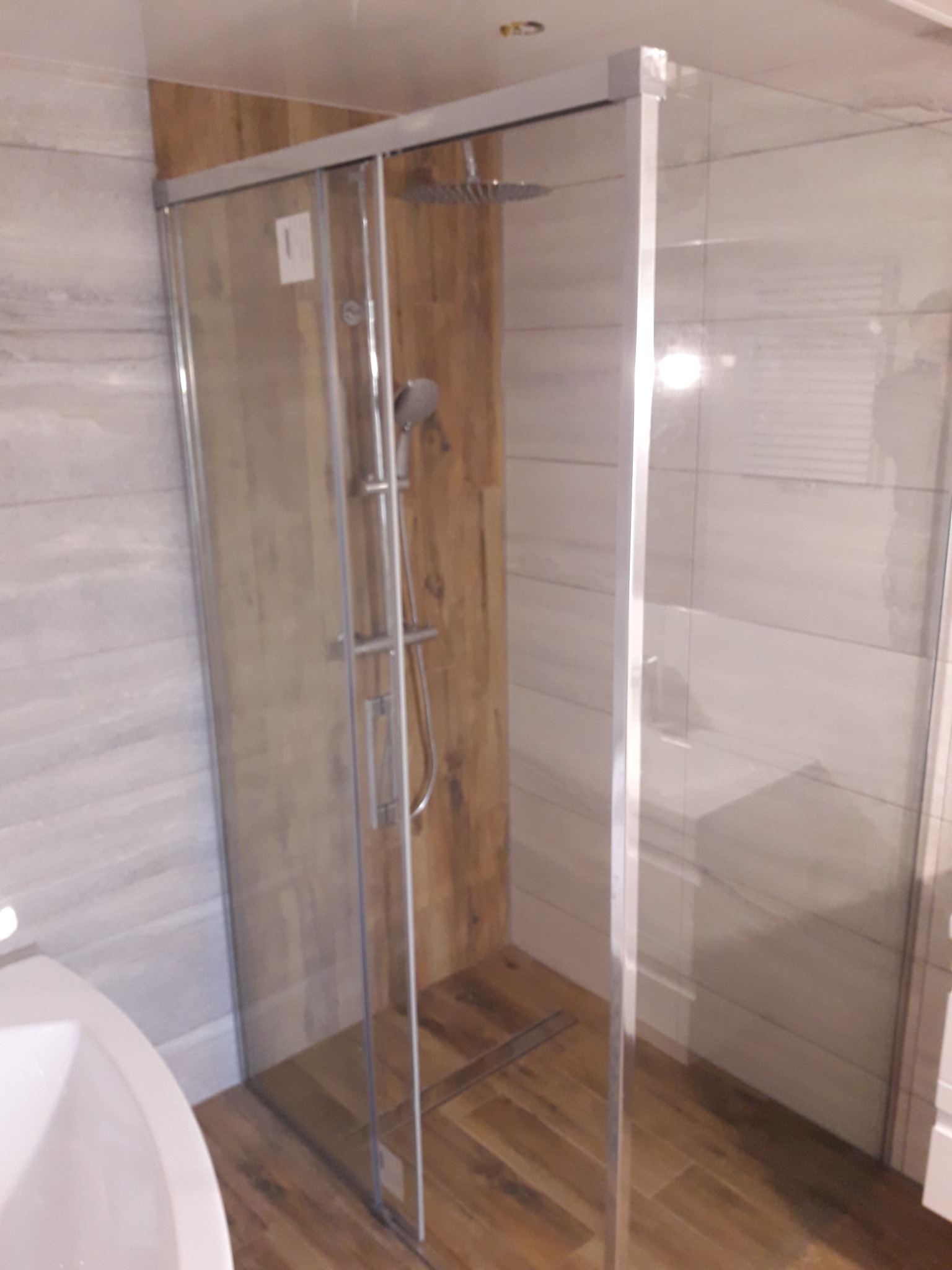 Nowoczesna kabina prysznicowa z deszczownicą i panelami imitującymi drewno, widoczny fragment umywalki.