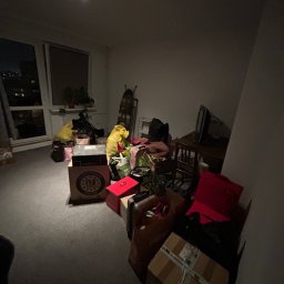 KA group Anton Kharin - Pokój przed przeprowadzką: kartony, torby i worki z rzeczami przygotowane do transportu, widoczne meble i okno z widokiem na miasto w tle.