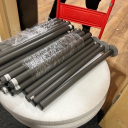 KA group Anton Kharin - Rury z metalowymi podstawami, owinięte folią, ułożone na okrągłym, białym siedzisku wózka transportowego z czerwonym uchwytem.