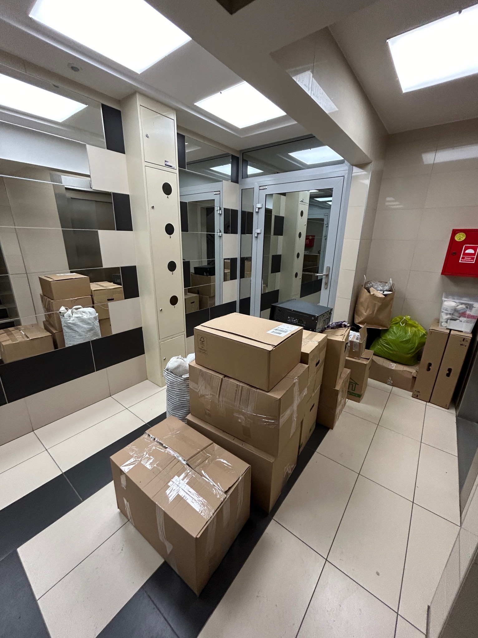 Kartonowe pudła i torby z rzeczami w korytarzu budynku, przygotowane do transportu podczas przeprowadzki.