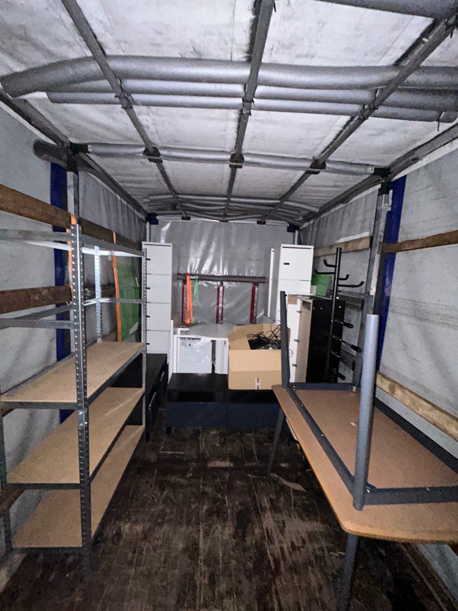 Wnętrze przestrzeni ładunkowej z zabezpieczonymi meblami i regałami, przygotowanymi do przewozu. Widoczne elementy wyposażenia mieszkania, kartony i zabezpieczenia.