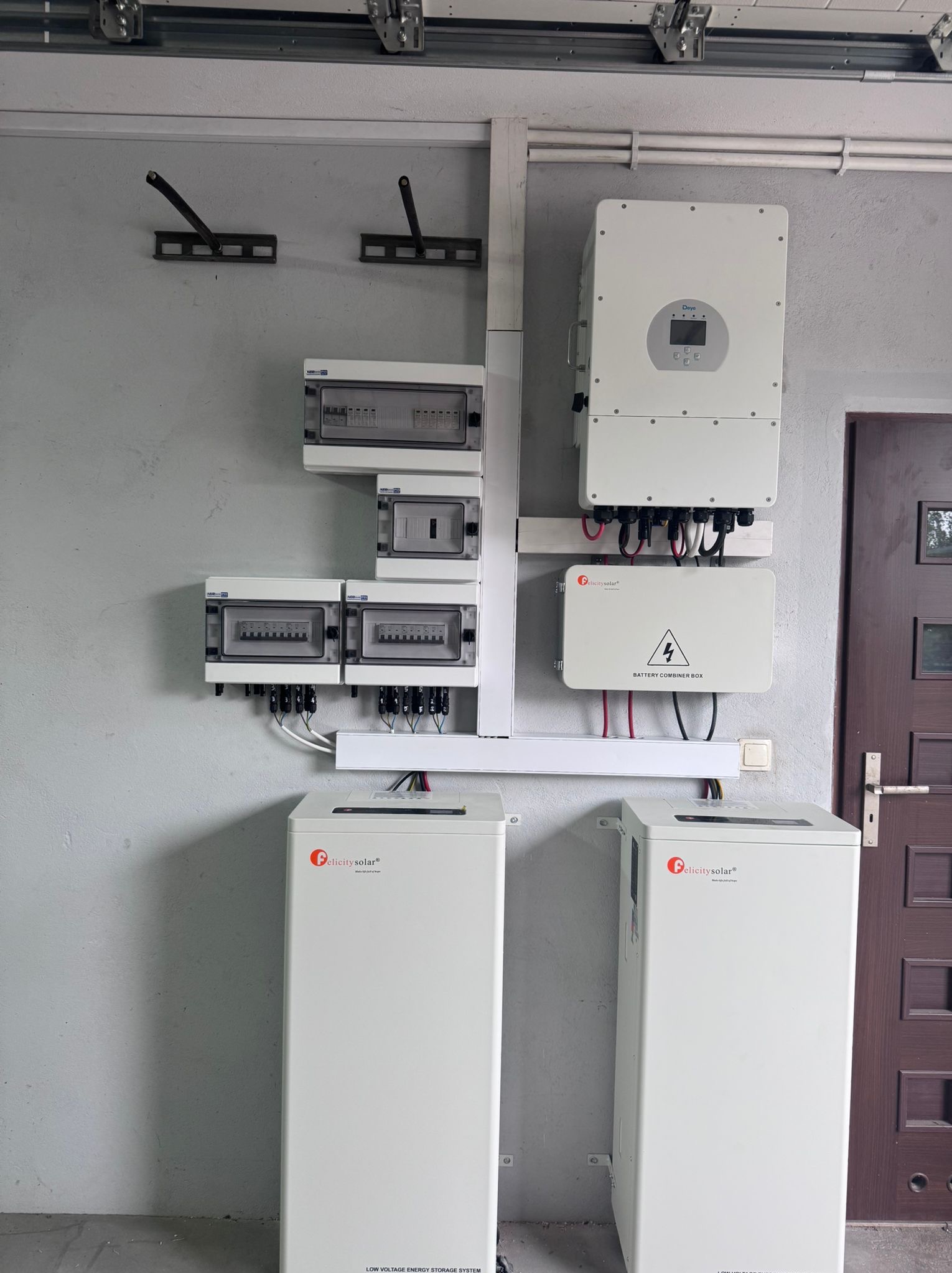 Kompletna instalacja fotowoltaiczna w garażu: białe akumulatory, inwerter, rozdzielnice. Widoczne kable i przewody. Montaż wykonany schludnie, estetycznie.