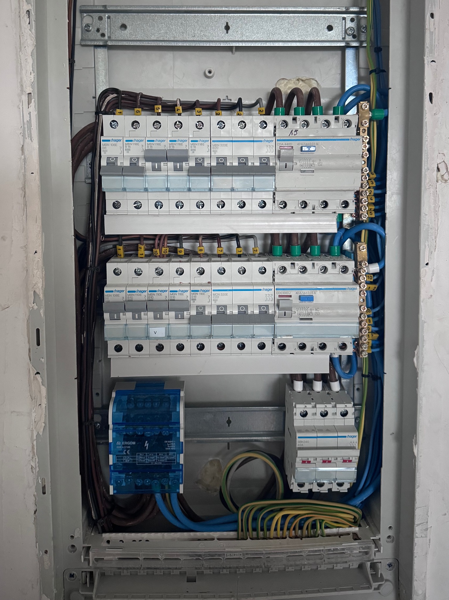 Rozdzielnica elektryczna Hager z zainstalowanymi bezpiecznikami i okablowaniem wewnątrz szarej obudowy, widok z bliska na elementy instalacji.