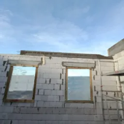 Wznoszenie ścian z bloczków betonu komórkowego z przygotowanymi otworami okiennymi, widoczne stalowe pręty zbrojeniowe nadproży oraz rusztowanie.