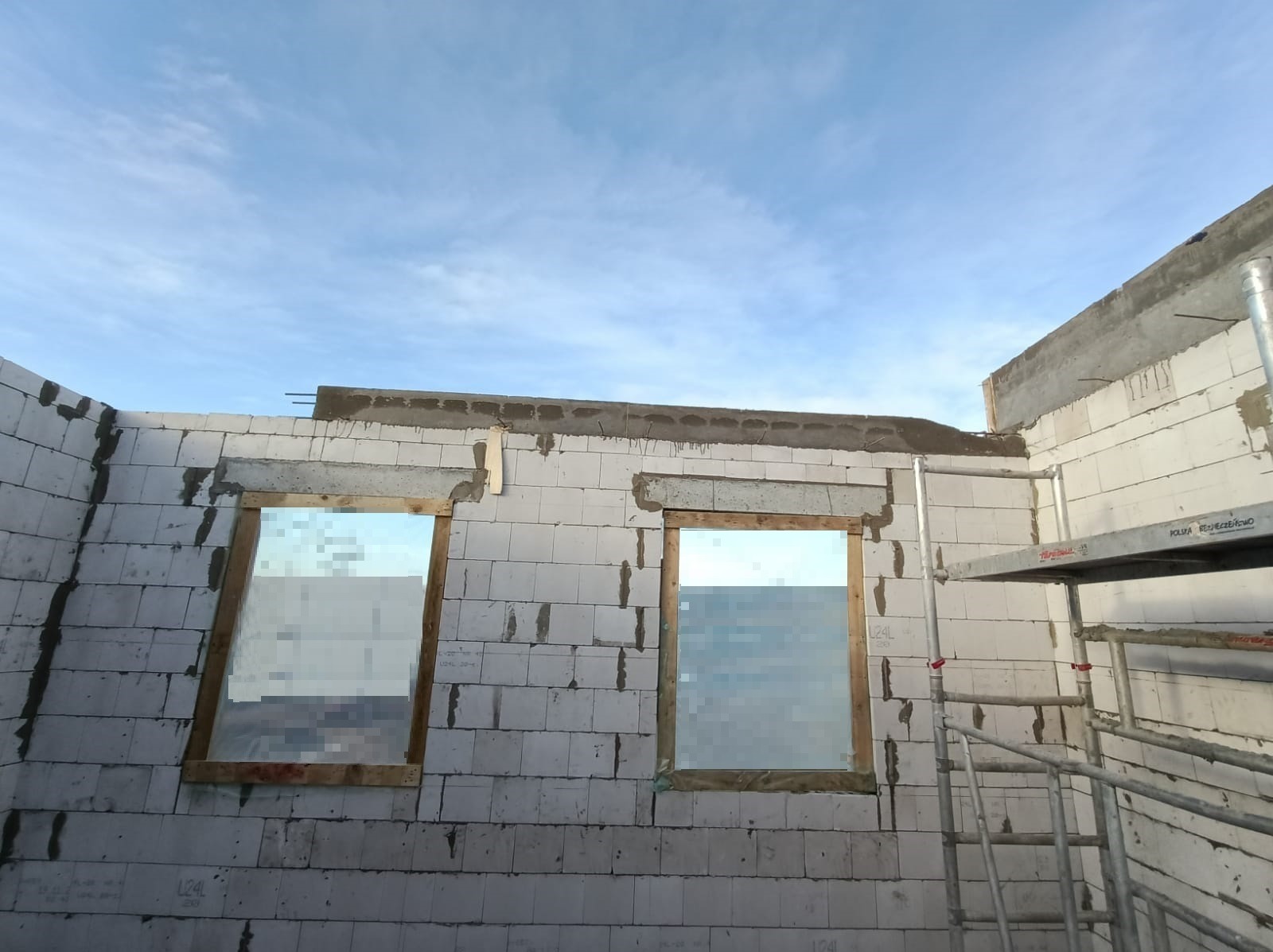 Wznoszenie ścian z bloczków betonu komórkowego z przygotowanymi otworami okiennymi, widoczne stalowe pręty zbrojeniowe nadproży oraz rusztowanie.