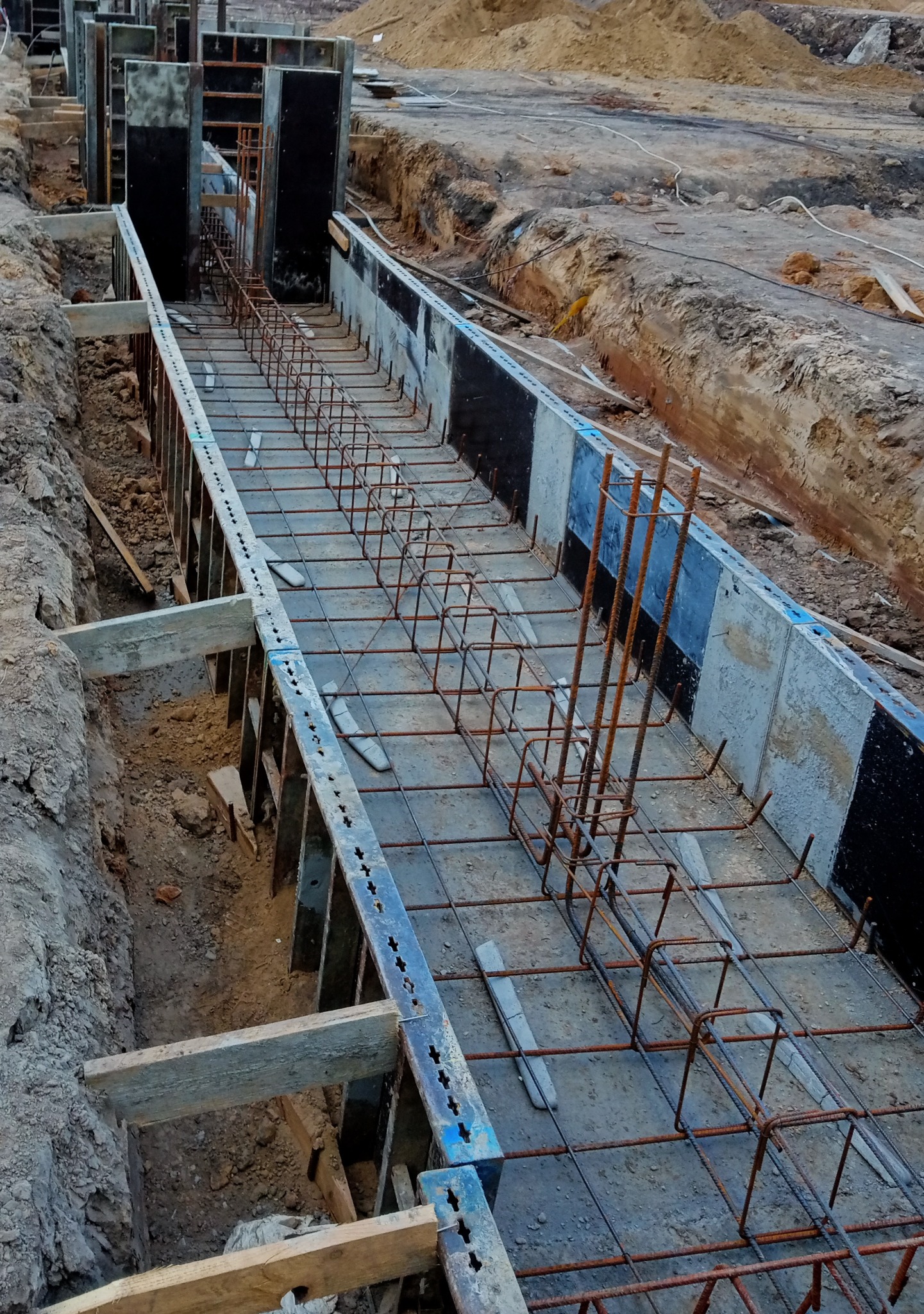 Przygotowanie zbrojenia w szalunku pod wylewkę fundamentów, widoczne wystające pręty zbrojeniowe.