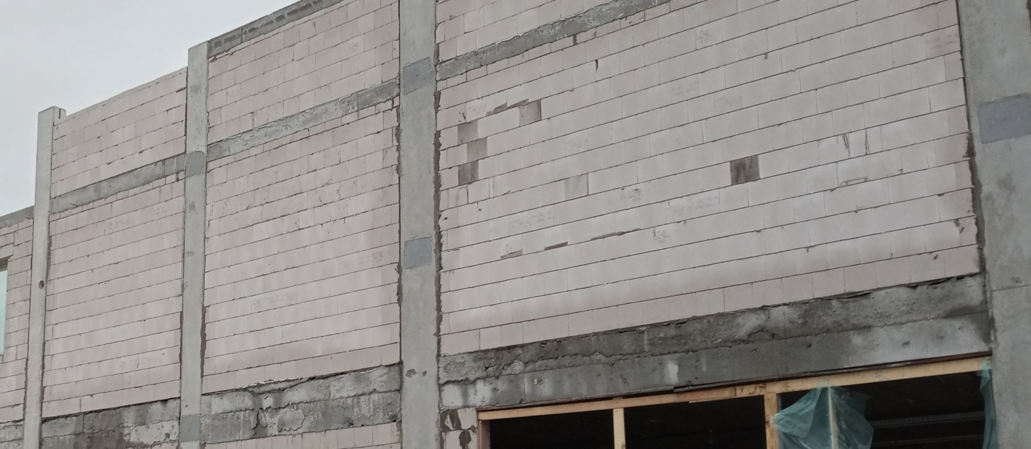 Wznoszenie ściany z białych bloczków betonu komórkowego z widocznymi spoinami i betonowymi słupami konstrukcyjnymi.